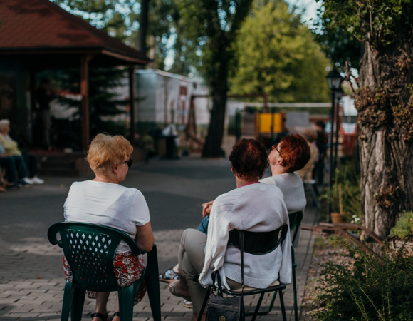 Na zdjęciu seniorki siedzące na ławce, tyłem do obiektywu