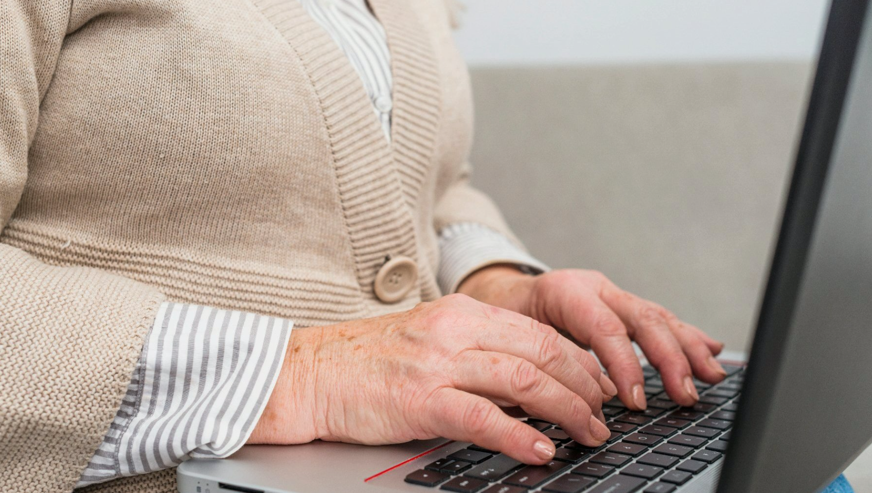 Na zdjęciu starsza kobieta pisząca coś na laptopie, widać tylko jej dłonie