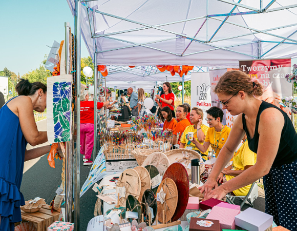 Na zdjęciu stoisko, po obu stronach ludzie, w tle banery organizacji pozarządowych