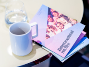 Na zdjęciu stół, na nim kubek i program festiwalu z napisem: zobacz więcej niż film