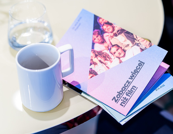 Na zdjęciu stół, na nim kubek i program festiwalu z napisem: zobacz więcej niż film