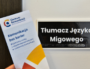Na zdjęciu tabliczka z napisem Tłumacz języka migowego i ulotka centrum komunikacji trzymana w dłoni