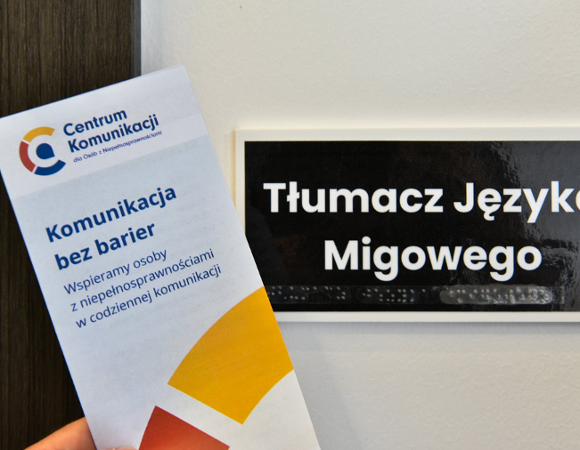 Na zdjęciu tabliczka z napisem Tłumacz języka migowego i ulotka centrum komunikacji trzymana w dłoni