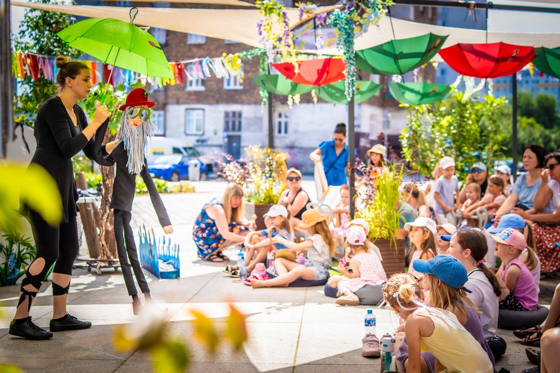 Na zdjęciu teatr uliczny, widać aktorkę i słuchające ją dzieci