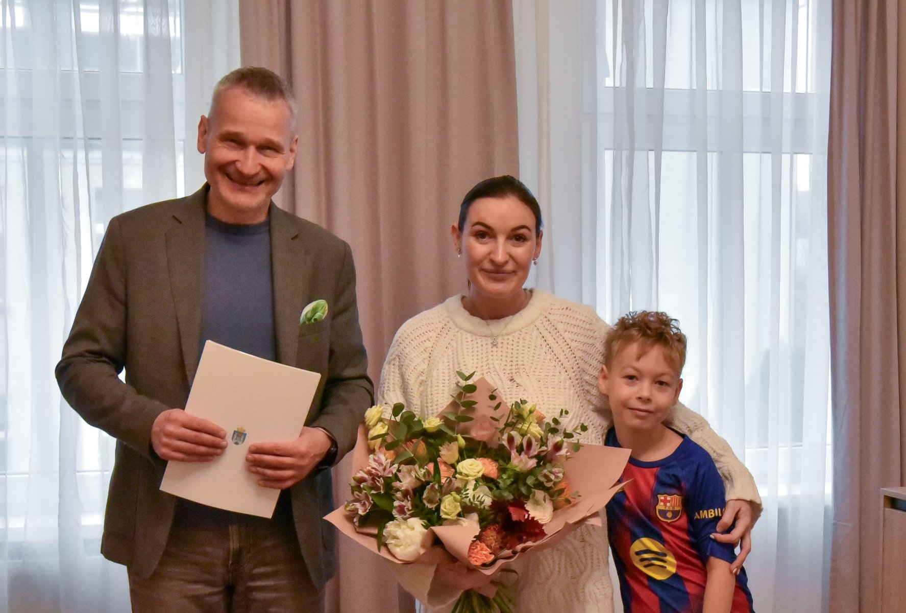 Na zdjeciu trzy osoby pozujące do aparatu - mężczyzna, kobieta i dziecko, kobieta trzyma kwiaty