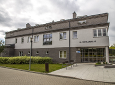 Na zdjęciu widać budynek przy ul. Drewlańskiej 10. Budynek ma 3 kondygnacje. Z prawej strony widać wejście do budynku. Jest przeszklone. Przed budynkiem znajduje się trawnik, chodnik i ławeczki.