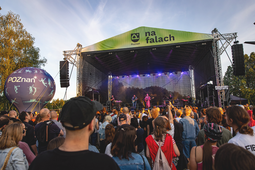 Na zdjęciu widać zespół występujący na scenie w Strzeszynku. Przed sceną stoi tłum ludzi. Z lewej strony granatowy balon z błękitnymi postaciami.