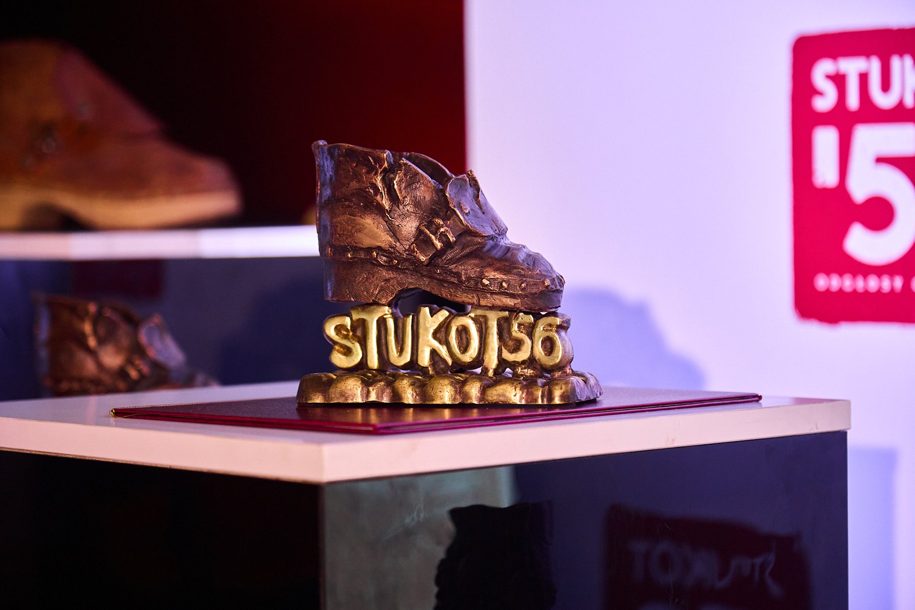 Nagroda Stukot '56 w kształcie drewnianego chodaka. Pod nim napis "Stukot '56". Nagroda jest wykonana z brązu. W tle prawdziwy but.