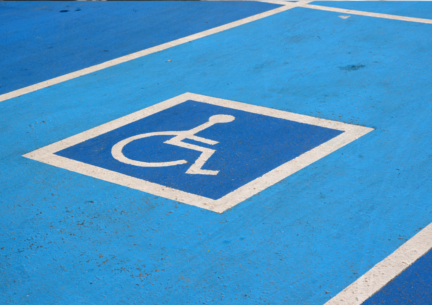 Niebieska powierzchnia parkingu z oznaczonym miejscem dla osób z niepełnosprawnościami.