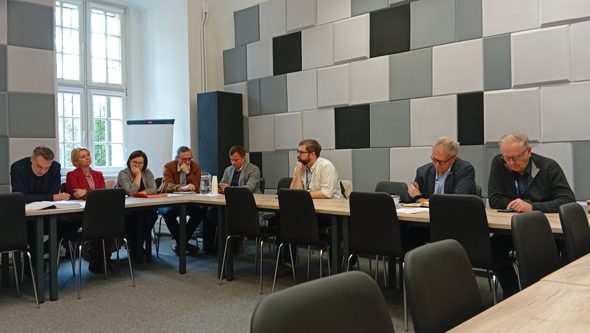 około kilkanaścioro osób siedzi za stołem konferencyjnym w sali - grafika artykułu