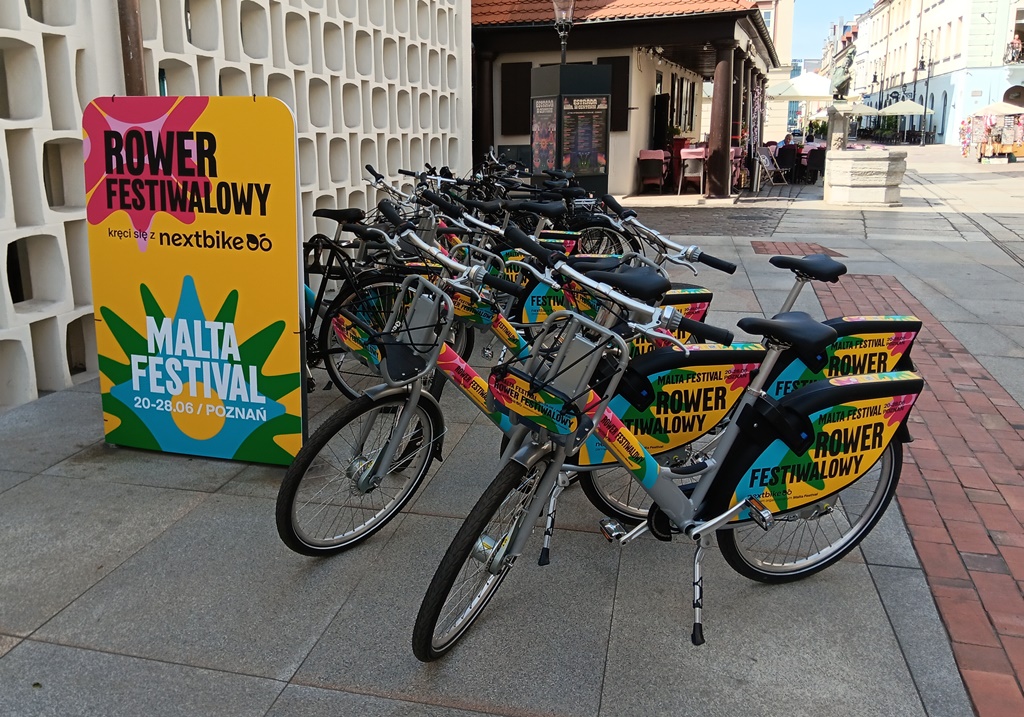 około kilkunastu rowerów miejskich ustawionych blisko siebie, obok baner z logo festiwalu malta, nextbike i napisem rower festiwalowy, rowery stoja na płycie Starego Rynku