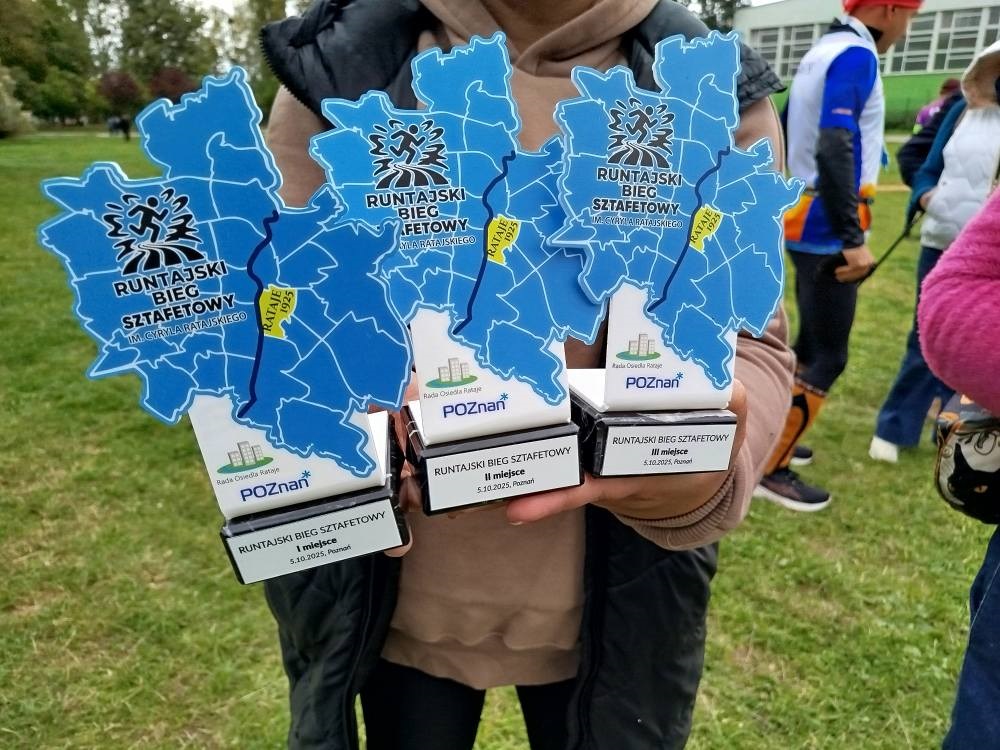 osoba niewidoczna na zdjęciu trzyma w ręku trzy statuetki z embelmatem w kształcie granic Poznania i napisem RUNTAJSKI BIEG SZTAFETOWY IM. CYRYLA RATAJSKIEGO