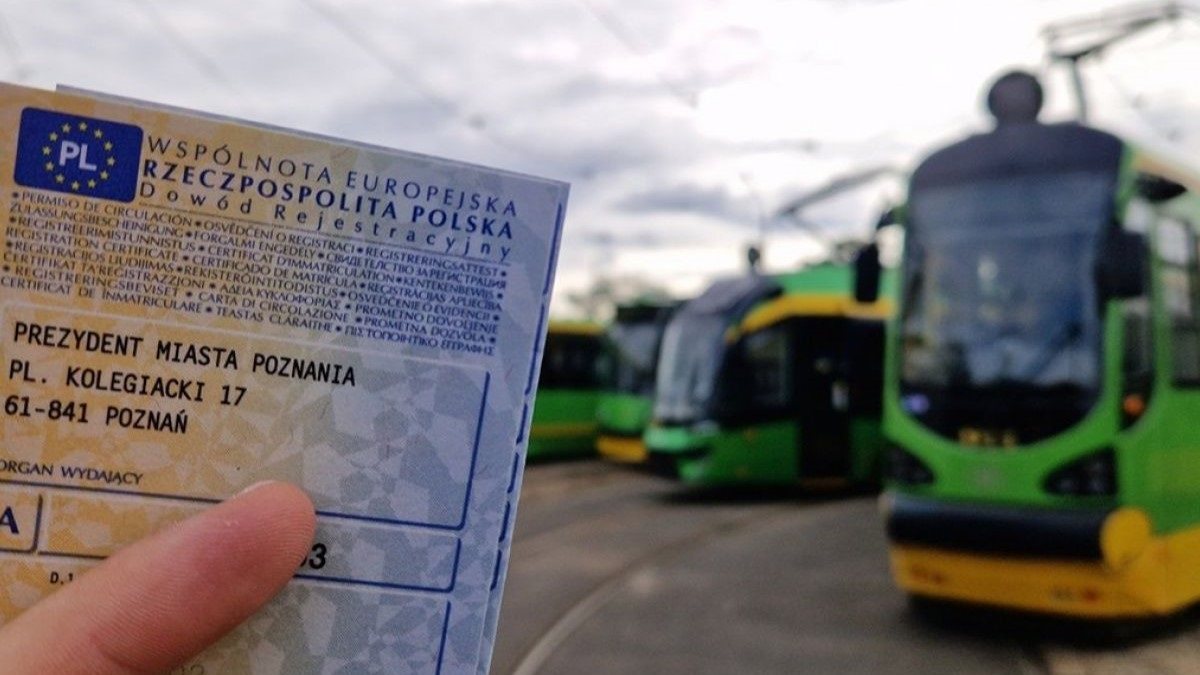 Osoba trzyma dowód rejestracyjny samochodu. W tle widać tramwaje
