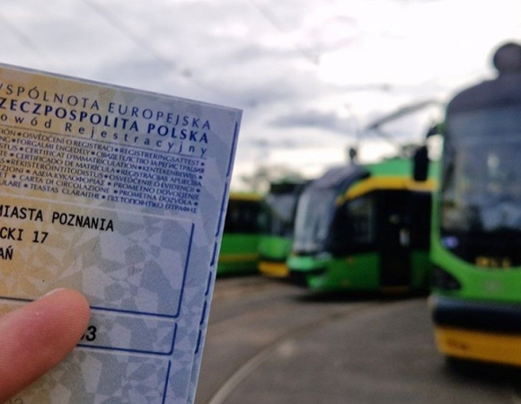 Osoba trzyma dowód rejestracyjny samochodu. W tle widać tramwaje
