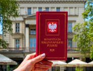 Osoba trzyma egzemplarz Konstytucji Rzeczypospolitej Polskiej. W tle budynek Arkadii przy Placu Wolności