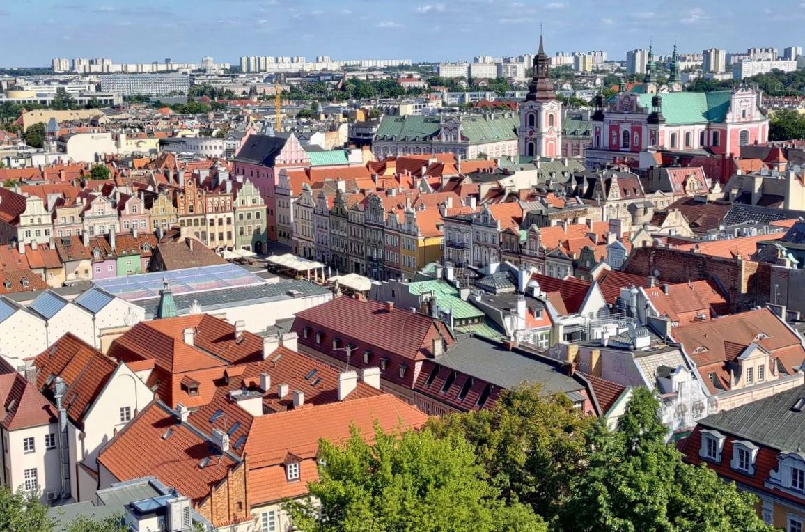 panorama miasta z lotu ptaka, na pierwszym planie zabudowa śródmiejska, wąskie kamienice ze spadzistymi dachami, widać wieże kościelne, na dalszym planie nowe budynki, bloki mieszkalne, biurowce, wieżowce