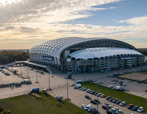 Panoromiczny widok na miejską zabudowę z charakterystyczną sylwetką stadionu piłkarskiego w tle.