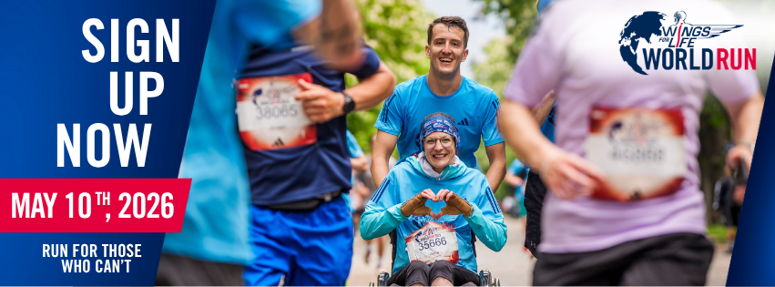 Plakat Wings for Life World Run, fot. Wings For Life World Run - mężczyzna prowadzi kobietę na wózku. W tle widać inne biegnące osoby