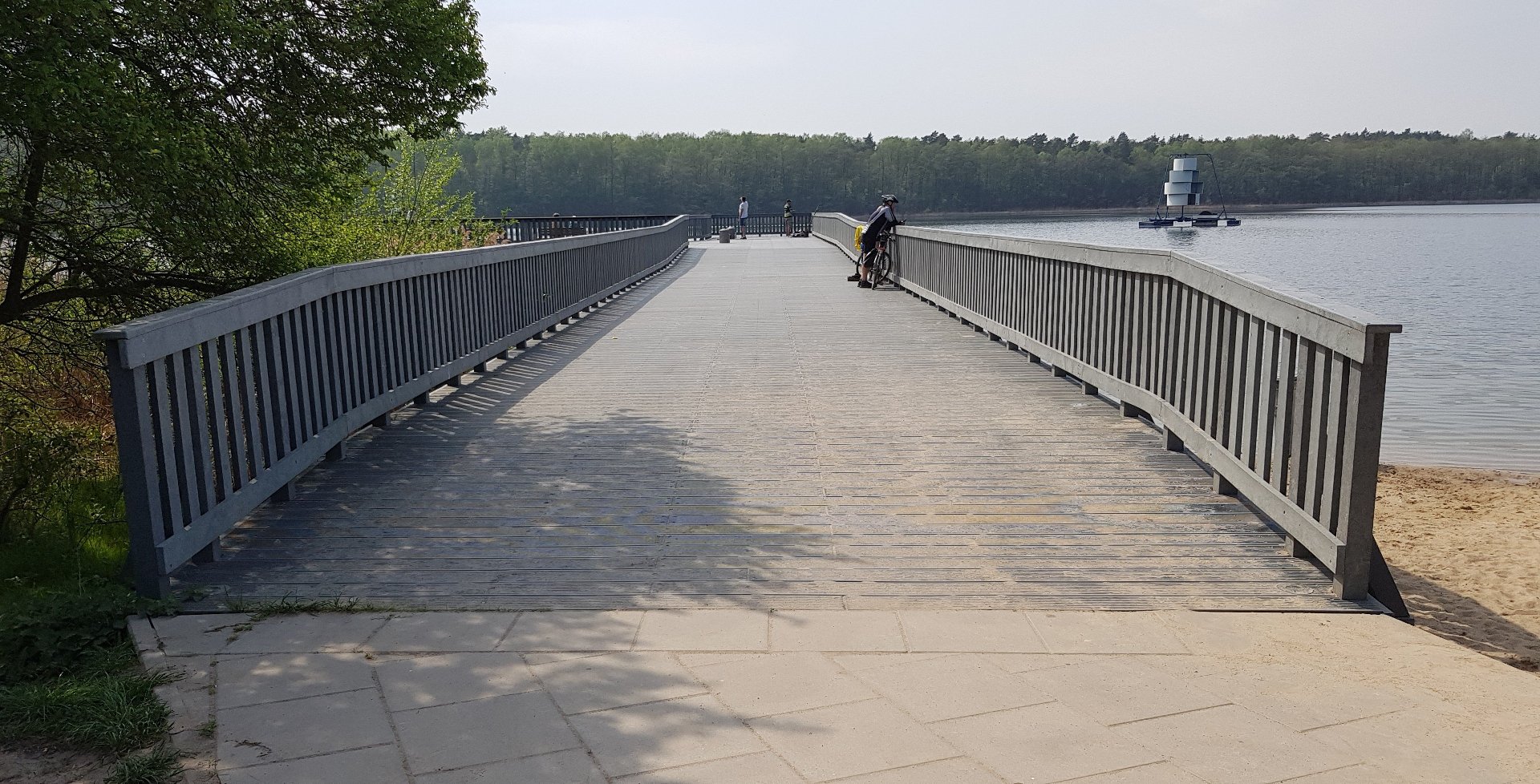 Pomost nad Jeziorem Strzeszyńskim, fot. POSiR - na pomoście widać rowerzystę i kilku pieszych, a w tle jezioro i las