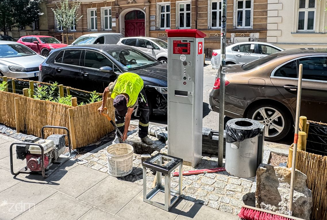 pracownik wykonuje prace związane z wykonaniem podstaw do montażu w chodniku nowych automatów parkingowych obok stoi stary automat
