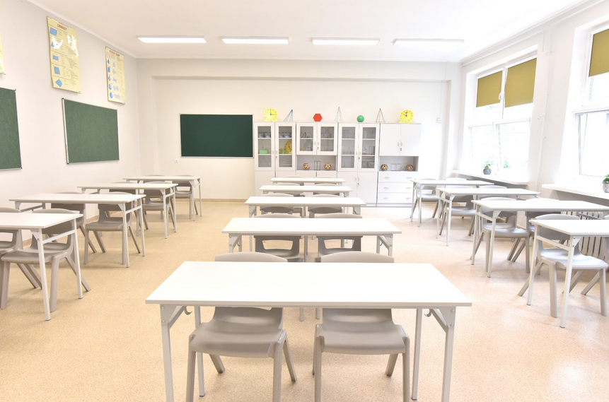 Pusta sala lekcyjna w szkole, ławki i krzesła, pod ścianą szafki i pomoce naukowe