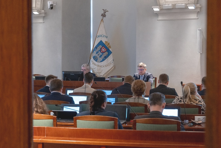 radne i radni, przed nimi stół prezydialny, przy nim dwie osoby, za nimi sztandar z herbem Poznania - grafika artykułu