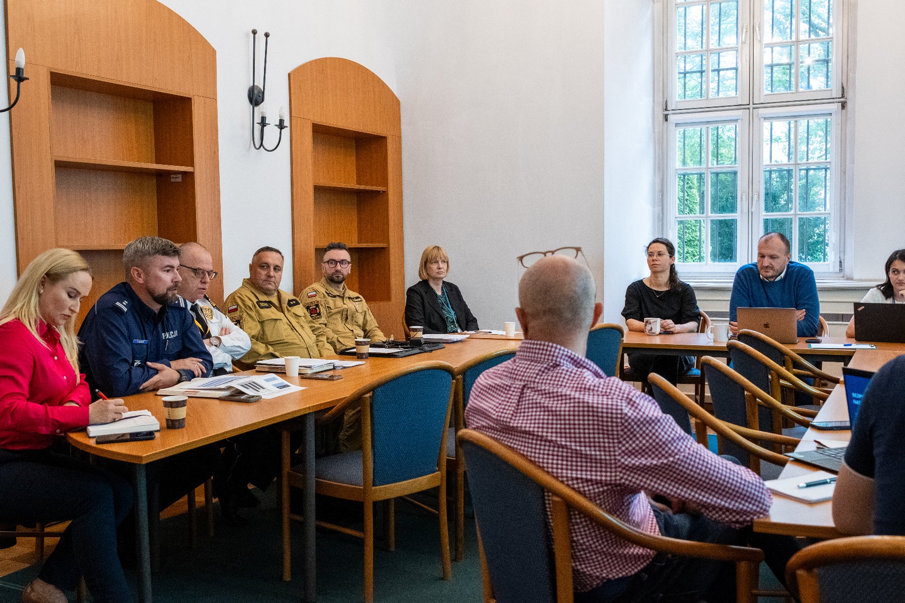 Radni siedzą wzdłuż stołów ustawionych w kształcie podkowy, w tle prezentacja.