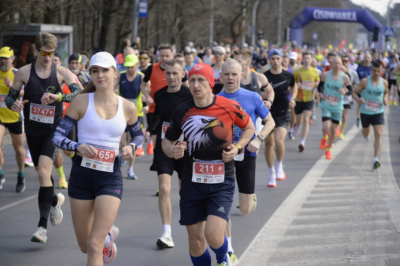 Recordowa Dziesiątka 2025, fot. Robert Woźniak/Głos Wielkopolski - tłum biegaczy biegnie ulicą po starcie biegu. Na pierwszym planie kobieta w białej koszulce i czapce oraz czarnych spodenkach oraz mężczyzna w czerwonej czapce i koszulce czarno-czerwonej z orłem