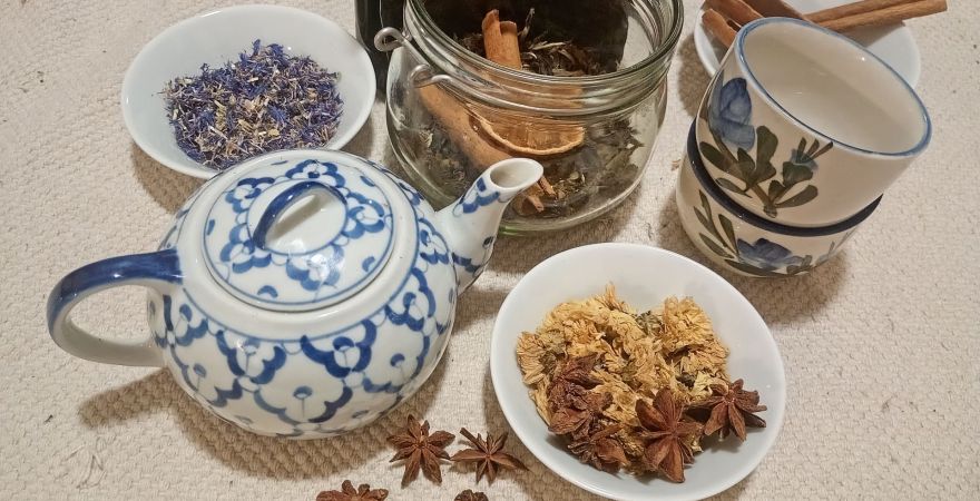 Różne mieszanki herbat w miseczkach, słoiczkach, obok imbryk i herbaciane filiżanki.