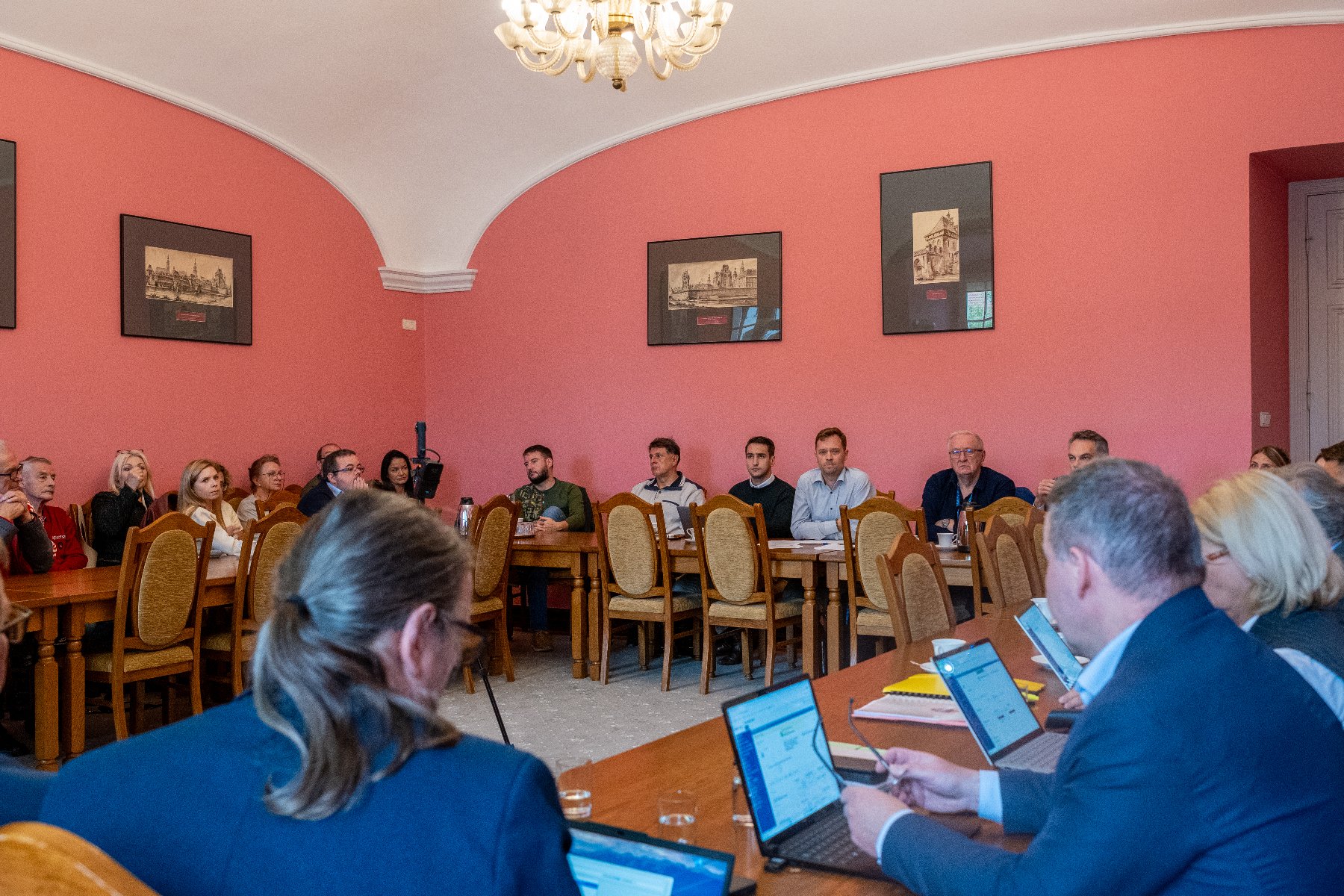 Sala posiedzeń, wypełniona ludźmi siedzącymi przy stołach.