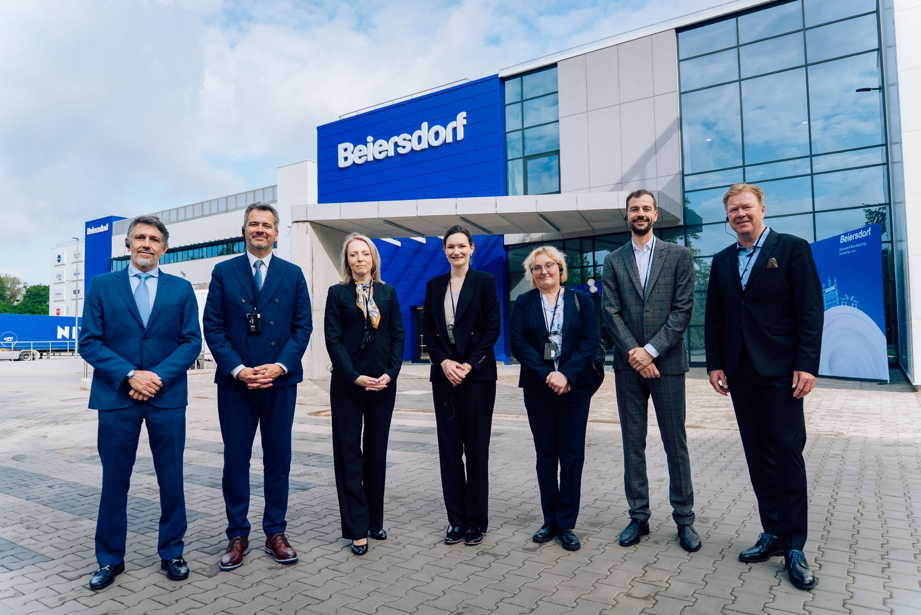 Siedem osób ubranych elegancko stojących przed fabryką Beiersdorf