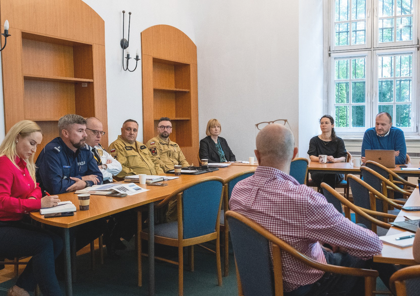 spotkanie w sali konferencyjnej kilkanście osób siedzi przy stole, wśród nich osoby w mundurach - grafika artykułu