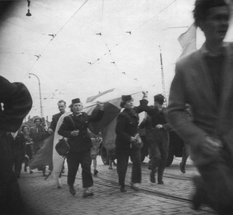 Stara fotografia kobiety w średnim wieku. Kobieta ma krótkie kręcone włosy. Spogląda z profilu w stronę obiektywu.