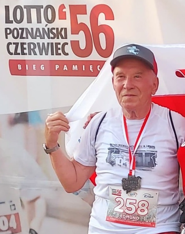 Starszy mężczyzna w stroju sportowym. Pozuje z medalem i flagą.
