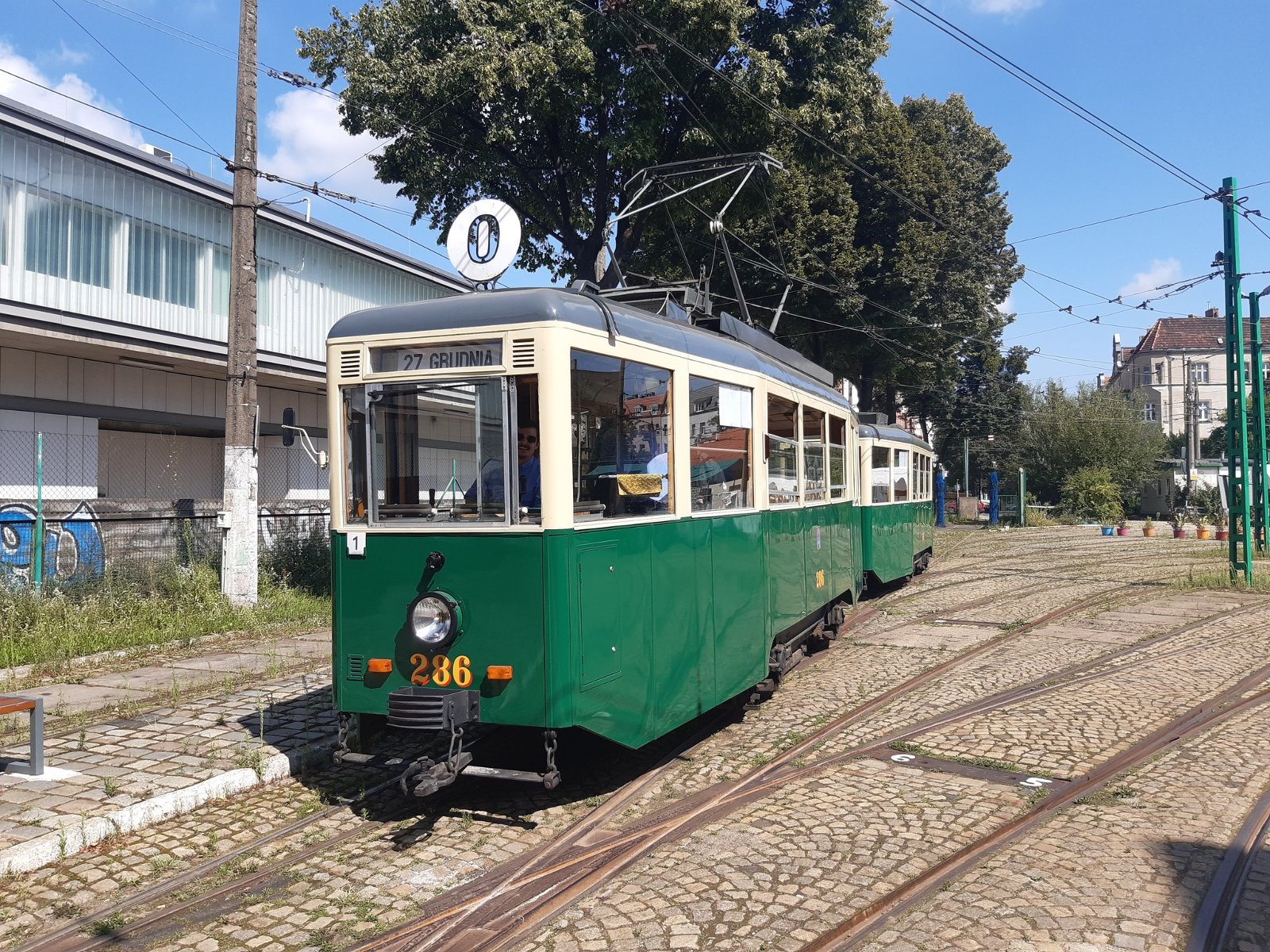 Stary, zabytkowy tramwaj z numerem 0 w kolorze zielonym stoi na pętli tramwajowej.