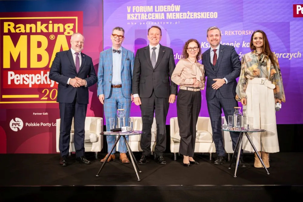 Sześć elegancko ubranych osób stoi na scenie podczas wydarzenia biznesowego, uśmiechając się do zdjęcia; w tle kolorowy baner "Ranking MBA"