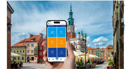 Telefon z otwartą aplikacją Smart City Poznań na tle ratusza.