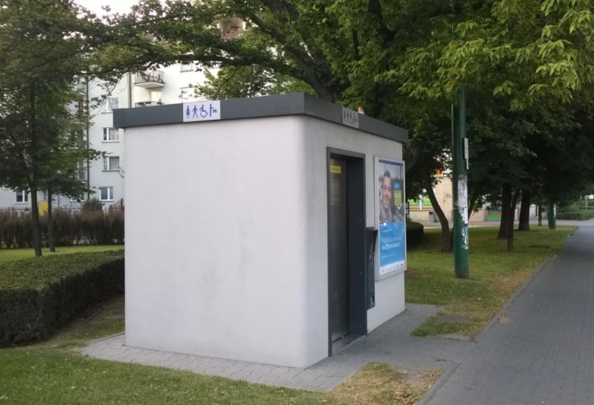 toaleta miejska automatyczna ustawiona przy chodniku obok ulicy z nia skwer