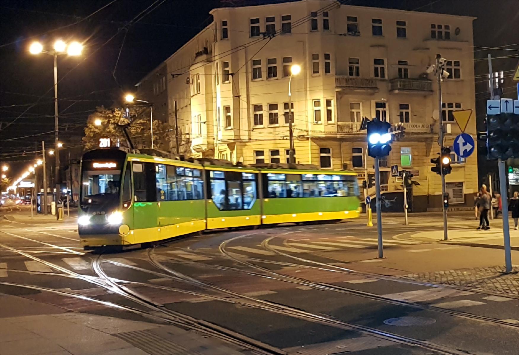 Tramwaj nadjeżający z prawej strony. Zdjęcie wykonane w porze nocnej. W tle kamienice.