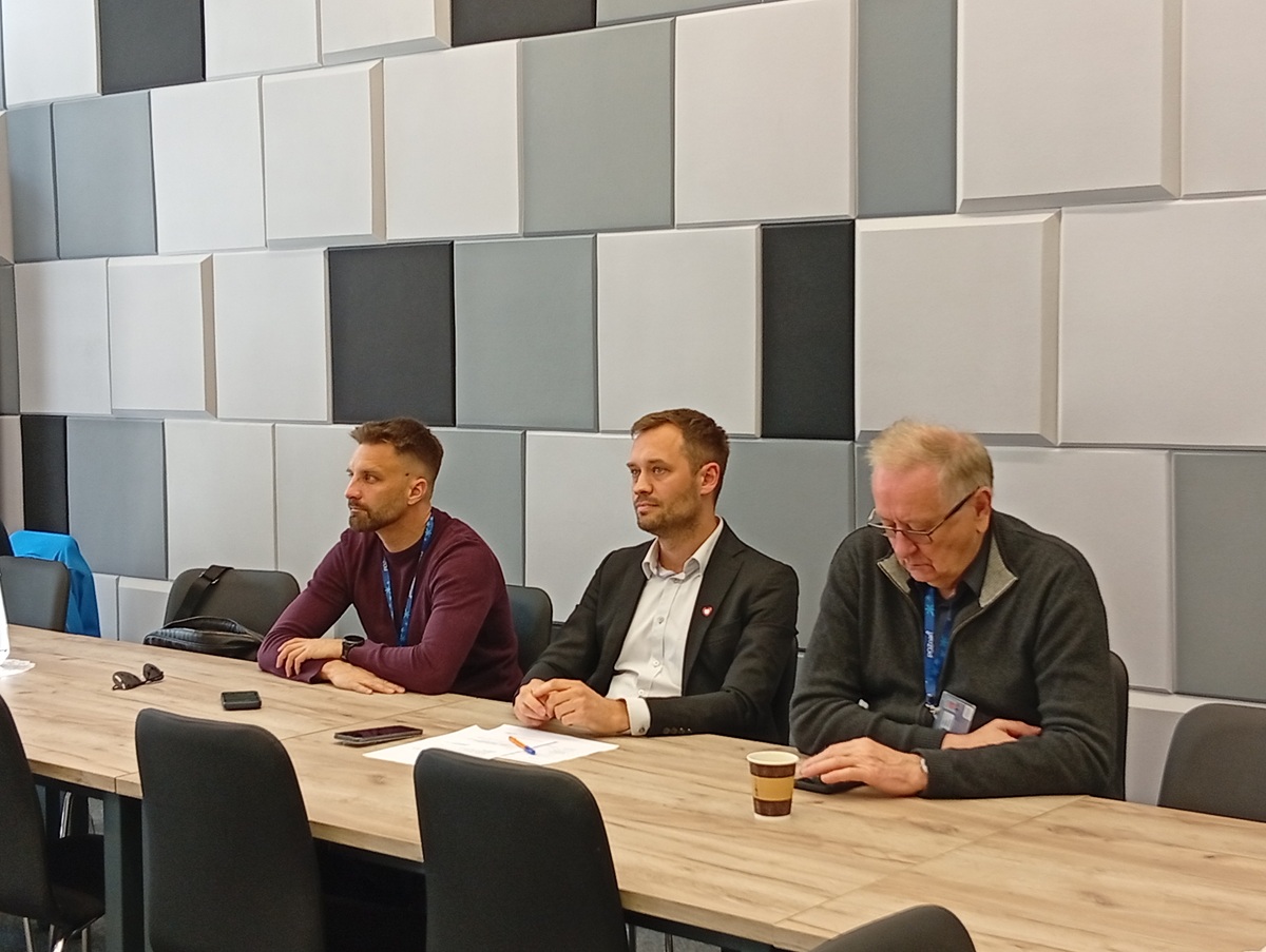 trzech mężczyzn siedzi za stołem w sali konferencyjnej - grafika artykułu