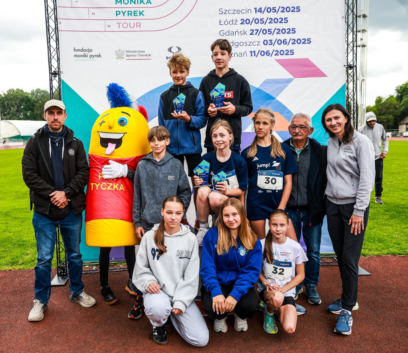Uczestnicy Monika Pyrek Tour 2025 w Poznaniu, fot. Adam Jastrzębowski - do zdjęć na tartanie ze statuetkami pozuje 3 chłopców i 4 dziewczynki, a także 2 mężczyzn i 1 kobieta, a także osoba przebrana za maskotkę zawodów