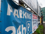 Ujęcie z bliska na pomarszczony, niebieski baner reklamowy, na którym białym kolorem widnieje duży napis w cudzysłowie: "PARKING 24h" i symbol litery P.