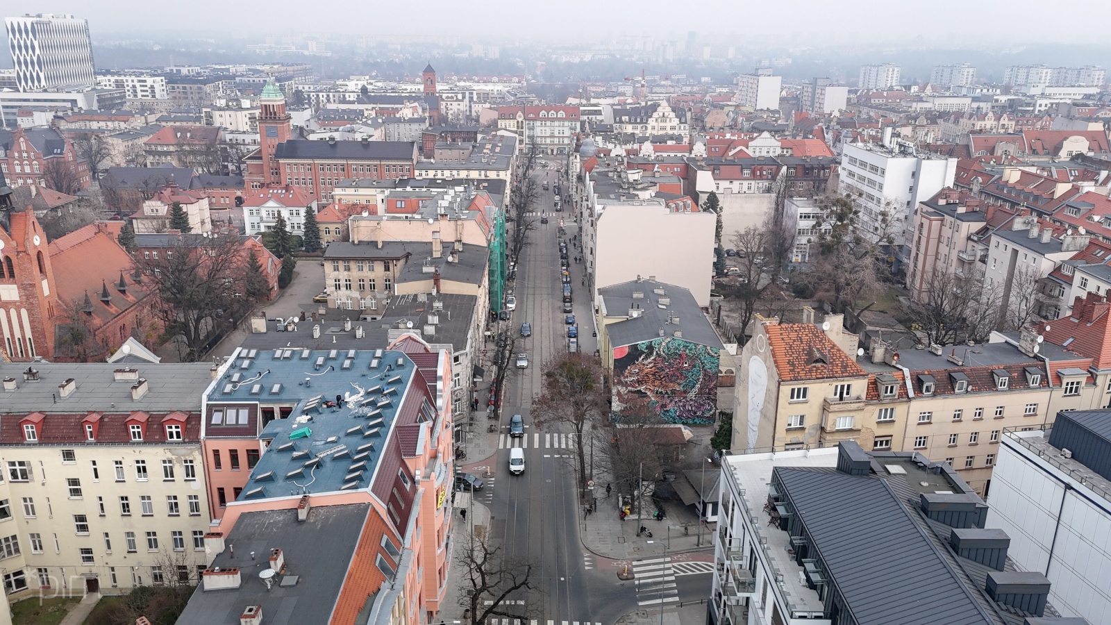 Ulica Kraszewskiego. Wokół widać kamienicw, budynek szkoły, a w tle kościół