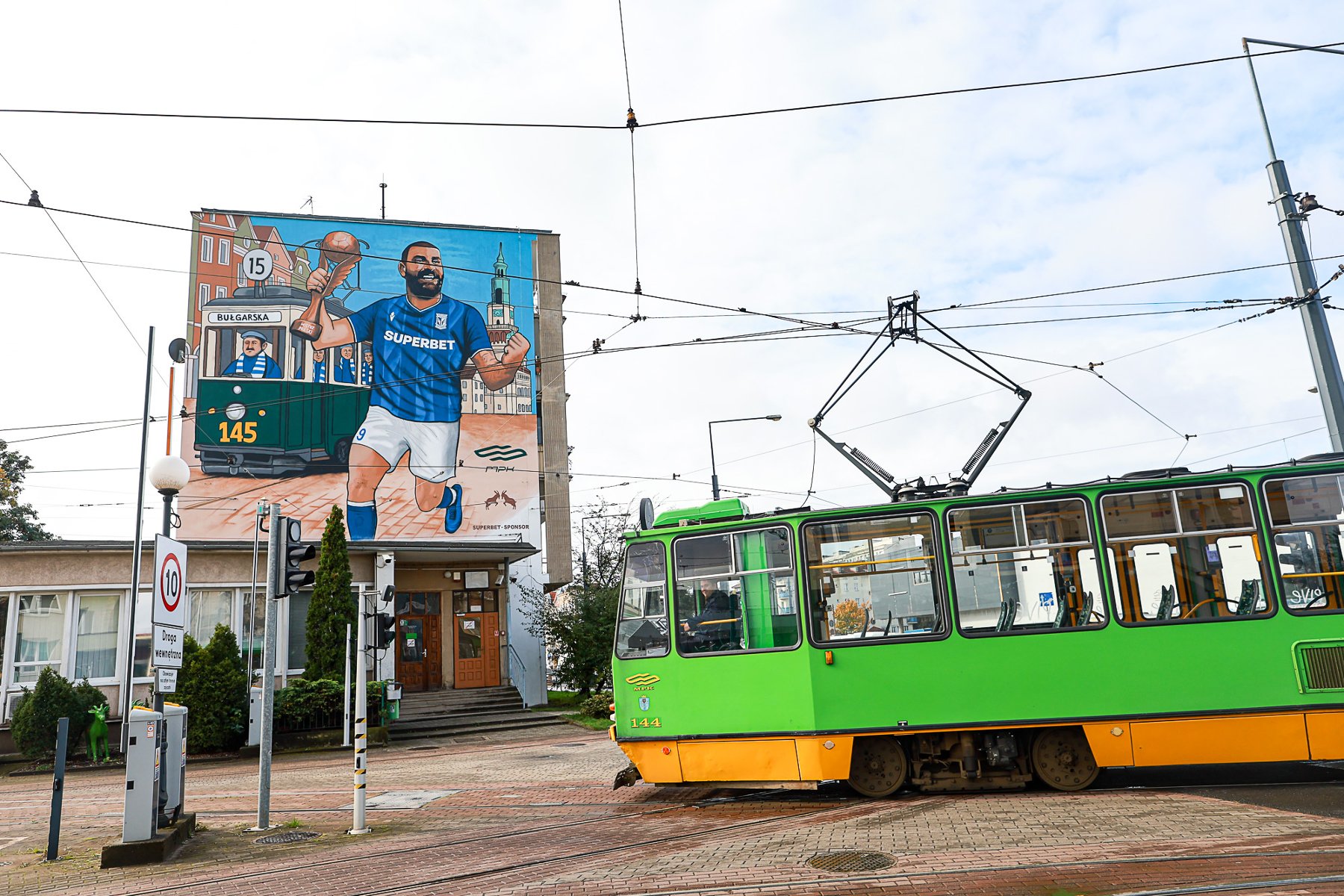 Uroczyste odsłonięcie upamiętniające 9. mistrzostwo Polski Lecha Poznań, fot. lechpoznan.pl/fot. Przemysław Szyszka - w tle mural z piłkarzem Lecha Mikaela Ishaka na ścianie budynku, a na pierwszym planie jadący tramwaj