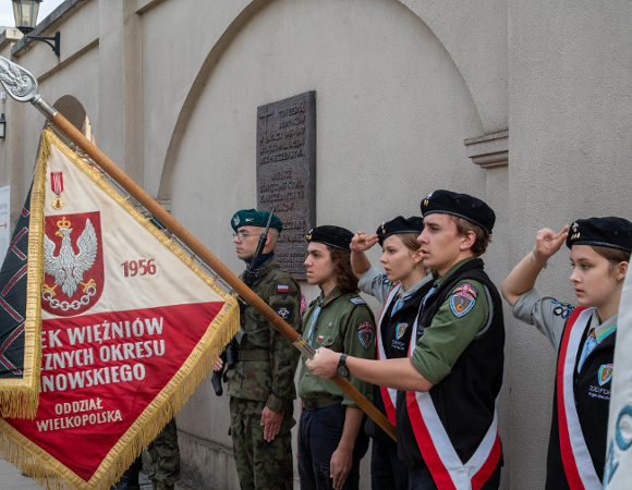 Uroczystość patriotyczna z udziałem pocztu sztandarowego Związku Więźniów Politycznych Okresu Stalinowskiego, harcerzy oddających honor oraz żołnierza stojącego na warcie przy tablicy pamiątkowej.
