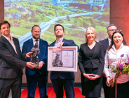 Uroczystość wręczenia nagrody architektonicznej z udziałem laureatów i przedstawicieli władz na tle prezentacji multimedialnej przedstawiającej panoramę inwestycji miejskiej.