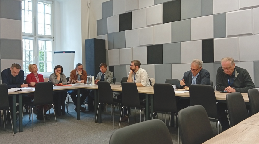 w sali za stołem konferencyjnym obraduje grupa około kilkunastu osób - grafika artykułu