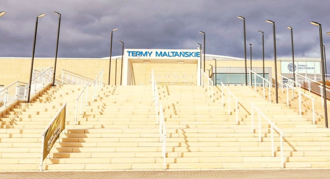 wejście do budynku Term Maltańskich, wysokie, szerokie schody, na ich szczycie wejście z dużym napisem nad nim TERMY MALTAŃSKIE, na schoda stoją latarnie