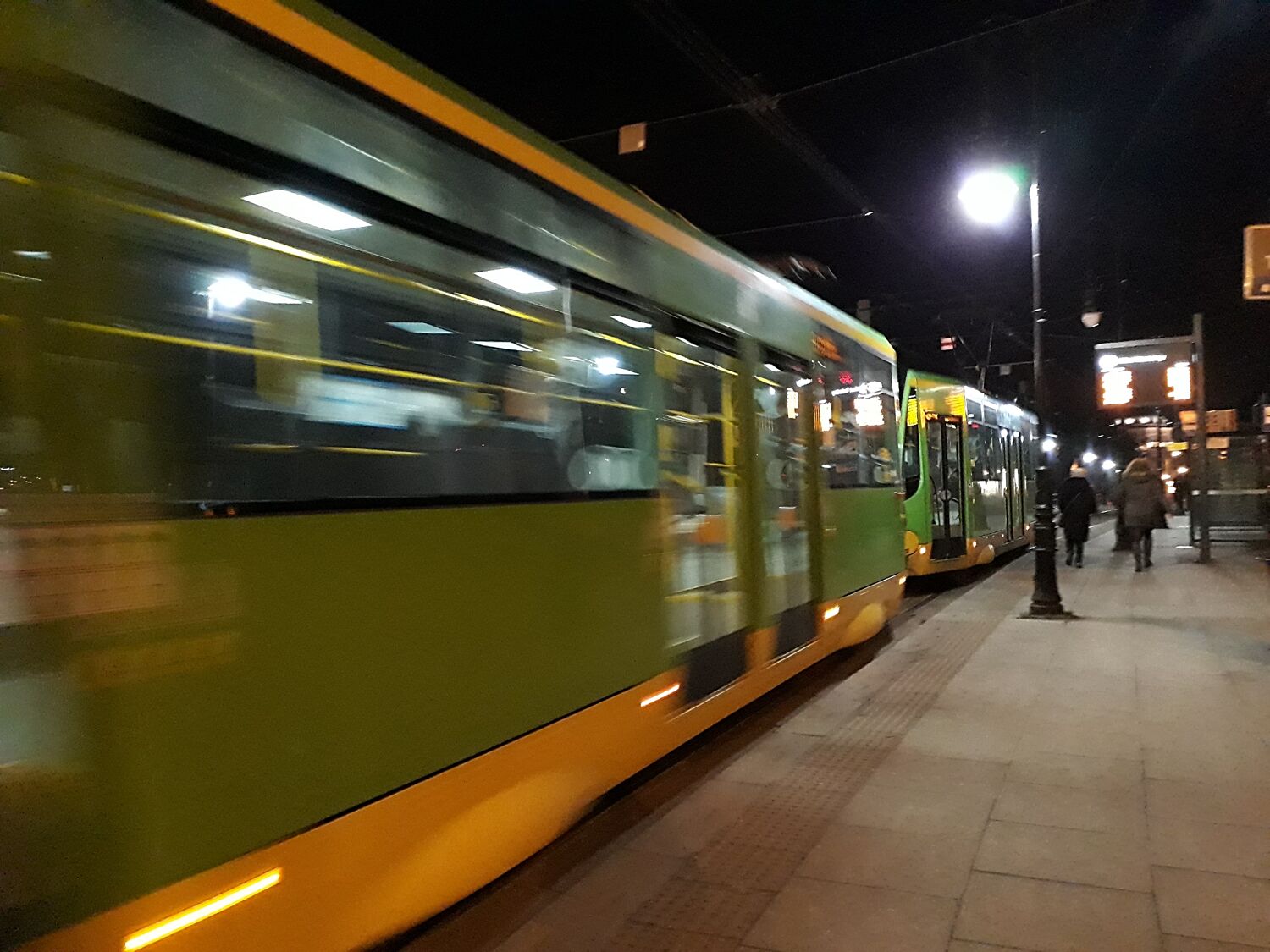 Widko z boku na jadący tramwaj w nocy Tramwaj koloru zielonego..