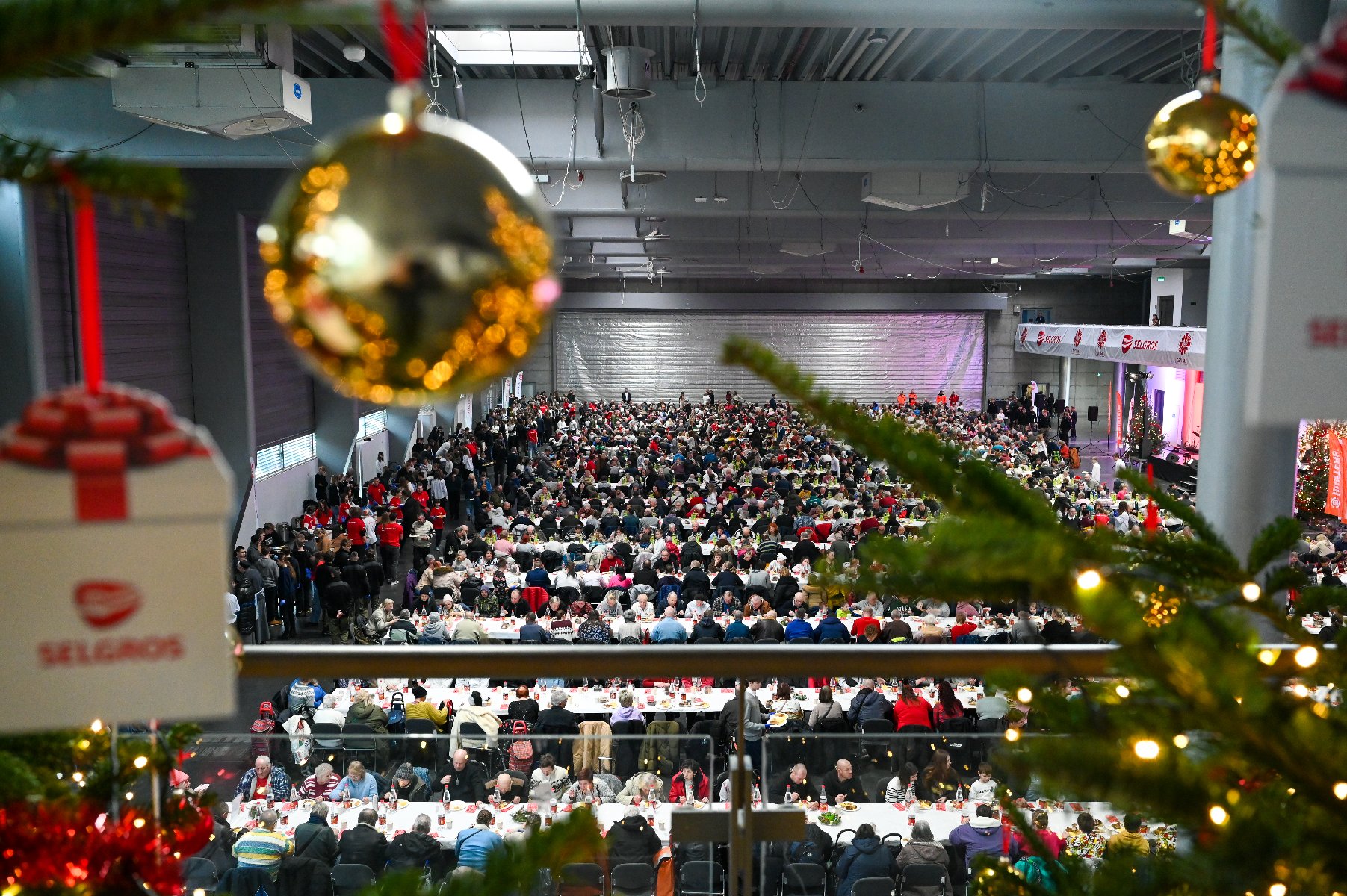 Widok na ludzi siedzących w hali MTP przy stołach podczas Wigilii Caritas